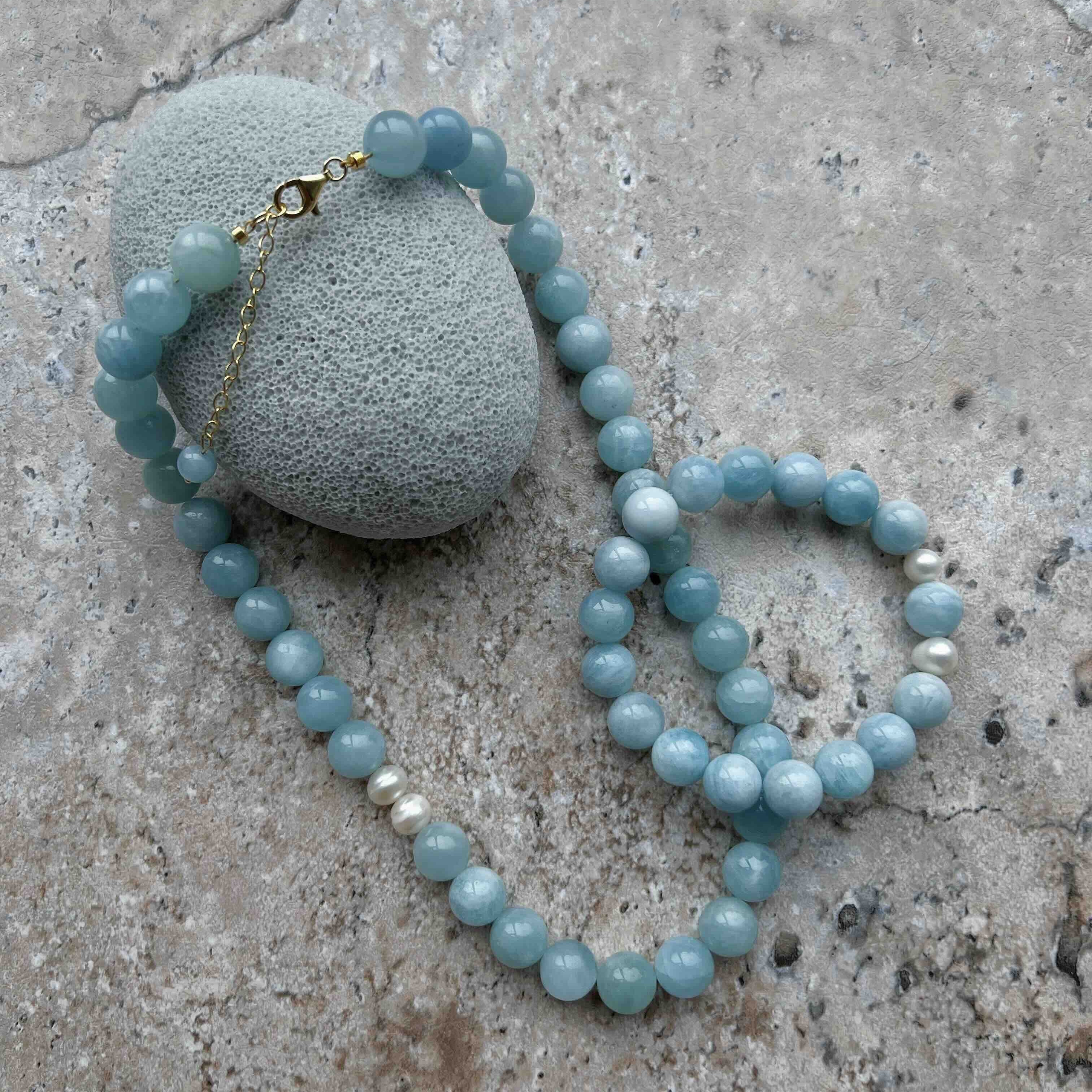 Aquamarine crystal necklace with round blue beads and freshwater pearls on a stone background – handmade gemstone jewelry for calm, clarity, and Throat Chakra healing