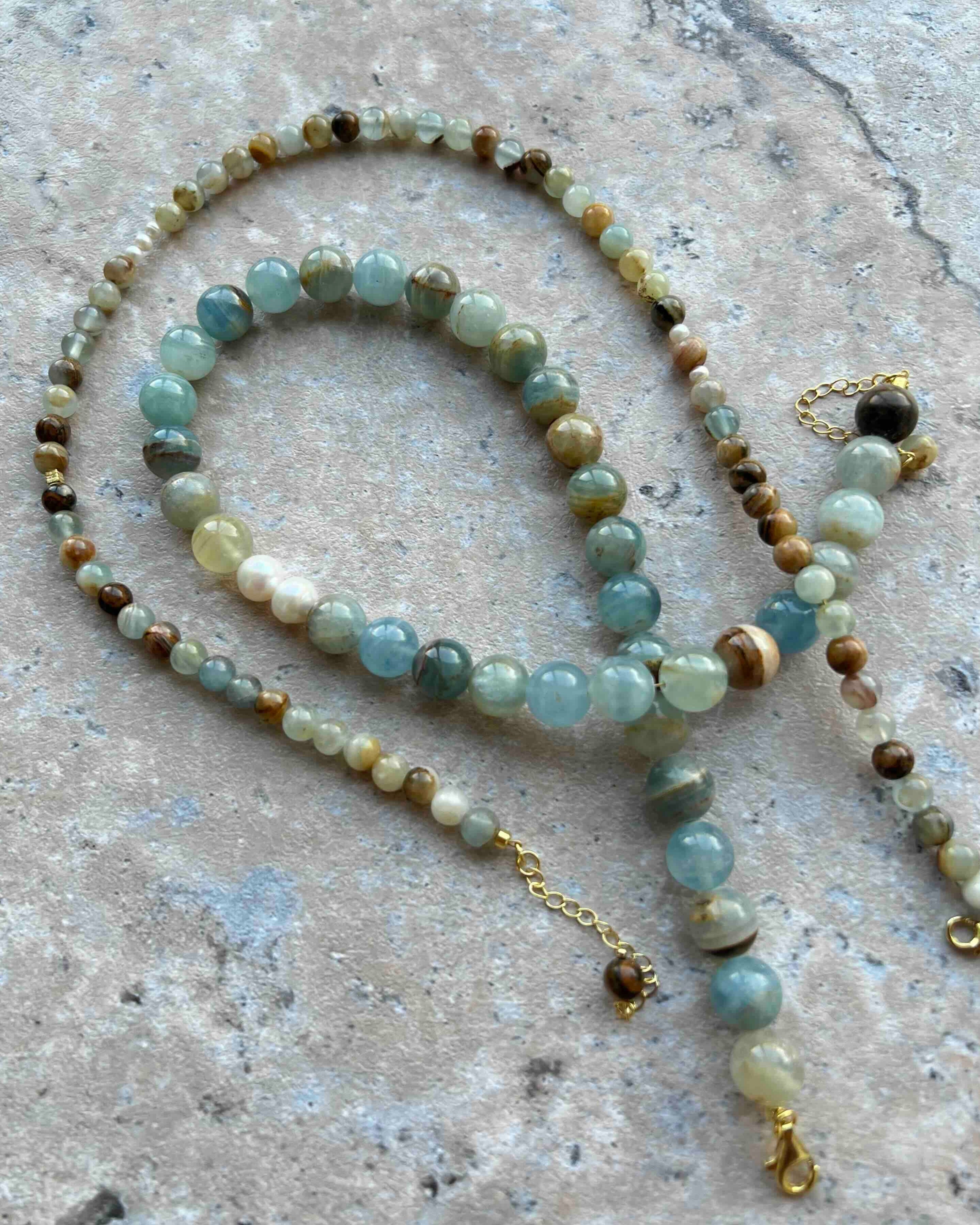 Blue Calcite bracelet and necklace set made with natural gemstone beads and gold details, displayed on a textured stone surface. The soft blue tones symbolize calm, clarity, and emotional healing.