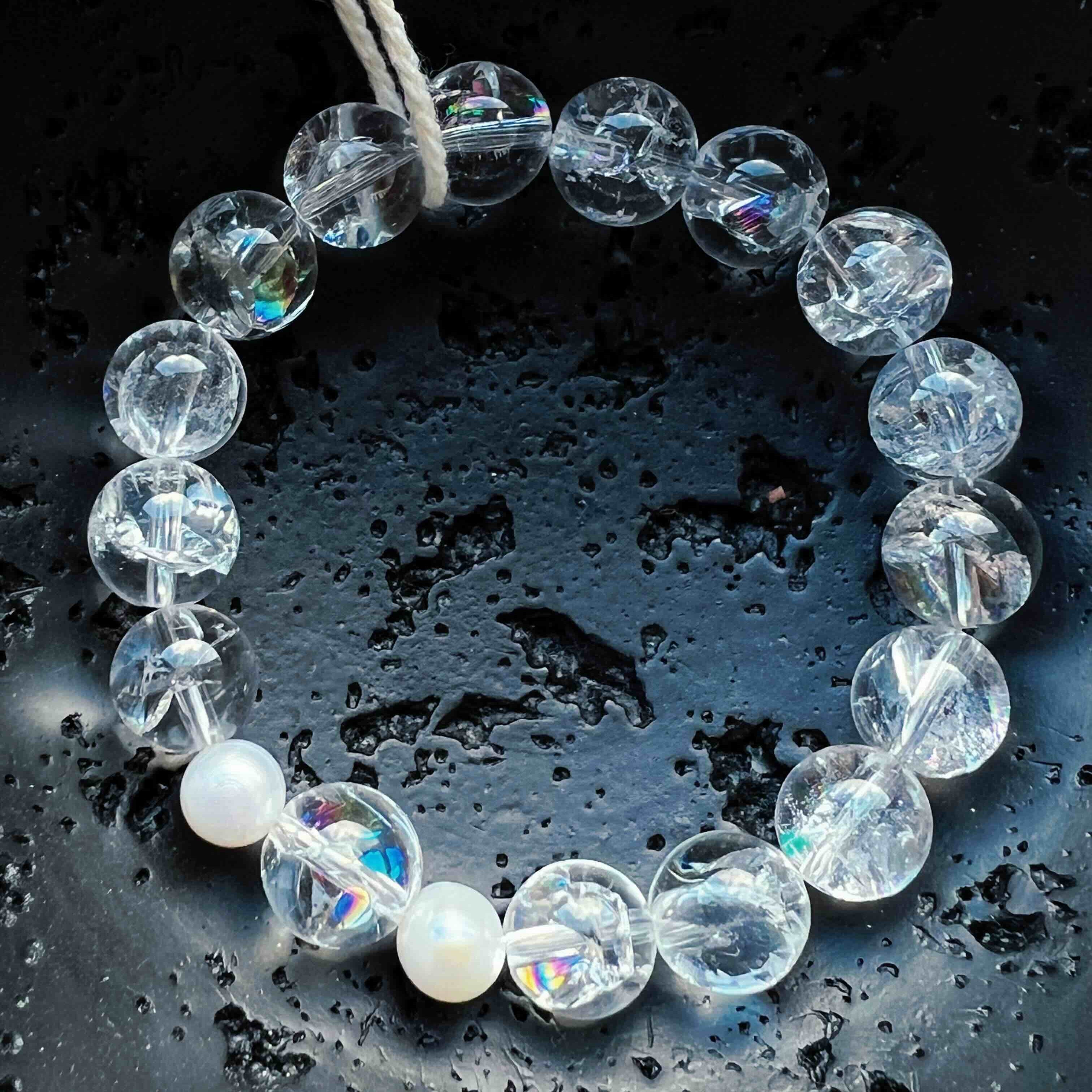 Clear Quartz bracelet featuring round transparent gemstones with natural rainbow inclusions, accented by freshwater pearls. Photographed on a dark textured surface with soft reflections, symbolizing clarity, healing energy, and light.