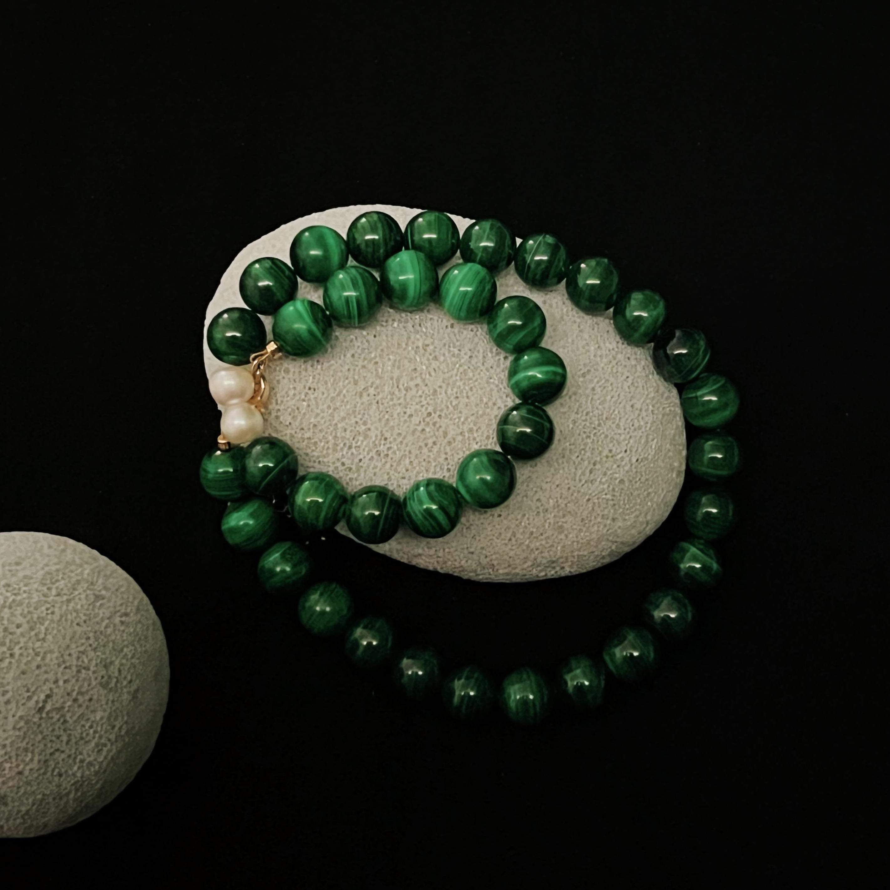 Malachite bracelet made with deep green natural gemstone beads and freshwater pearls, displayed on stone with a dark background. Symbolizing protection, transformation, and heart chakra healing.