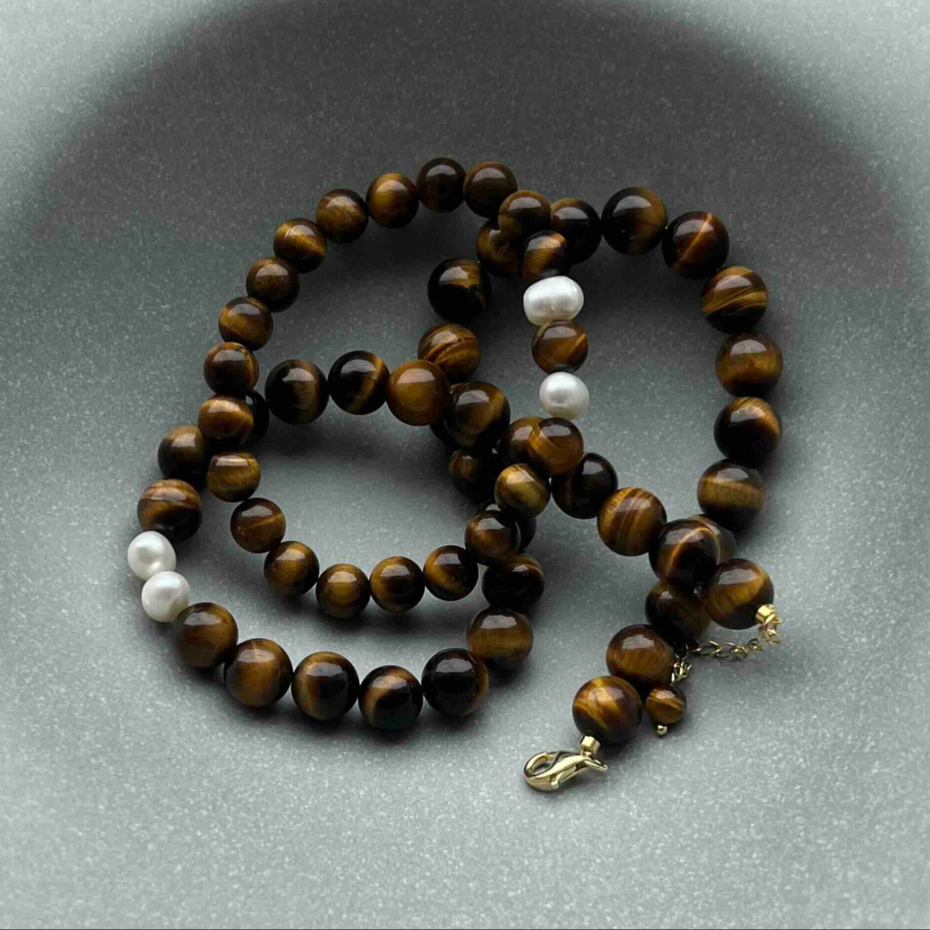 Tiger’s Eye crystal bracelet with golden-brown beads and freshwater pearls, displayed on a gray ceramic dish – handmade gemstone jewelry for confidence, protection, and grounding
