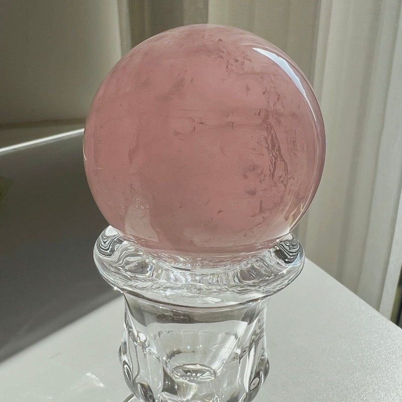 Pink crystal ball on a clear glass stand against a neutral background