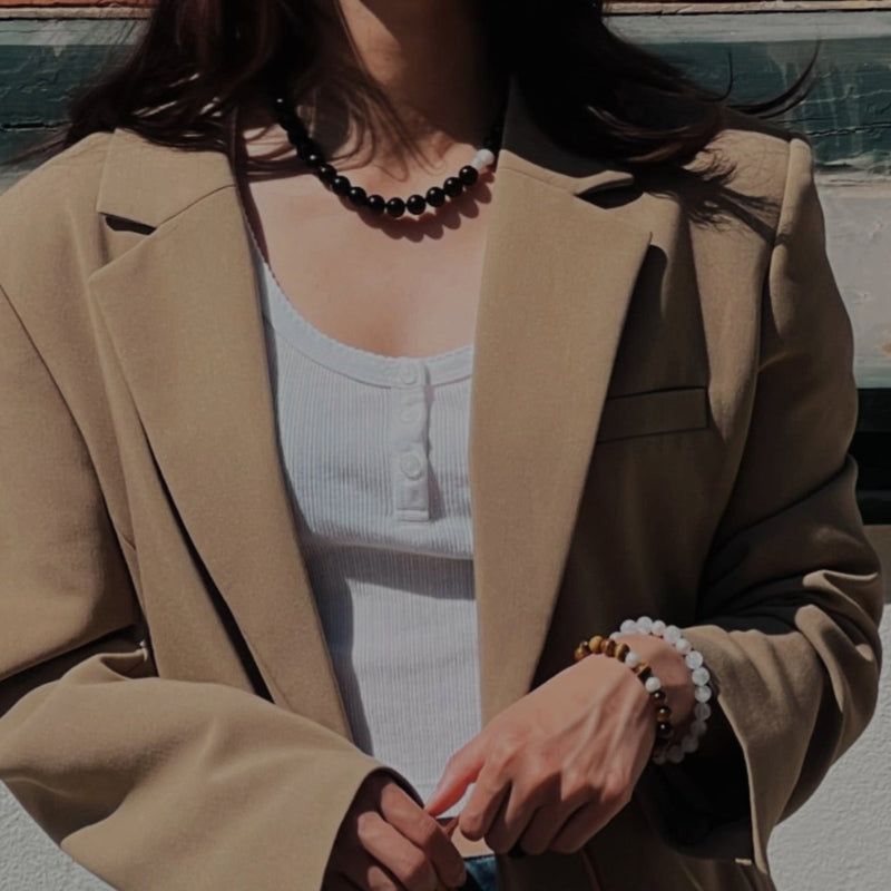 Person wearing a beige blazer and blue jeans, holding a patterned handbag against a plain background.