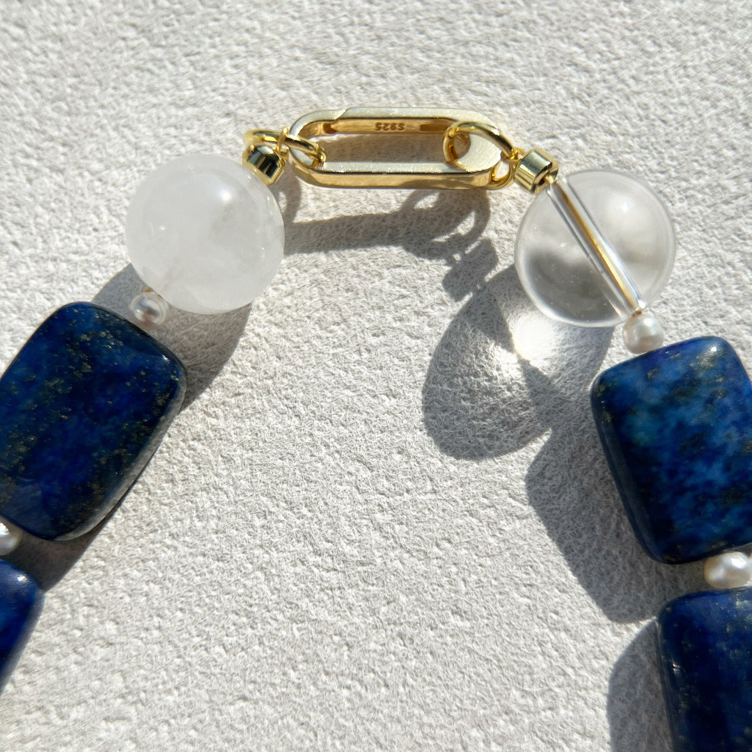 Macro detail of the Amaré Qinghua necklace featuring a signature gold-plated carabiner clasp with an S925 hallmark, connecting deep blue lapis lazuli, misty white jade, and clear quartz beads.