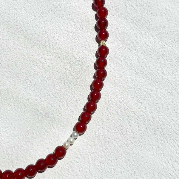 Close-up of the Red Agate Freya Necklace showing polished 6mm red crystal beads with subtle gold accents and freshwater pearls, highlighting its natural texture and warm tones.