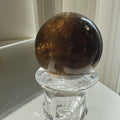 Smoky quartz sphere  on a stand with a plain background