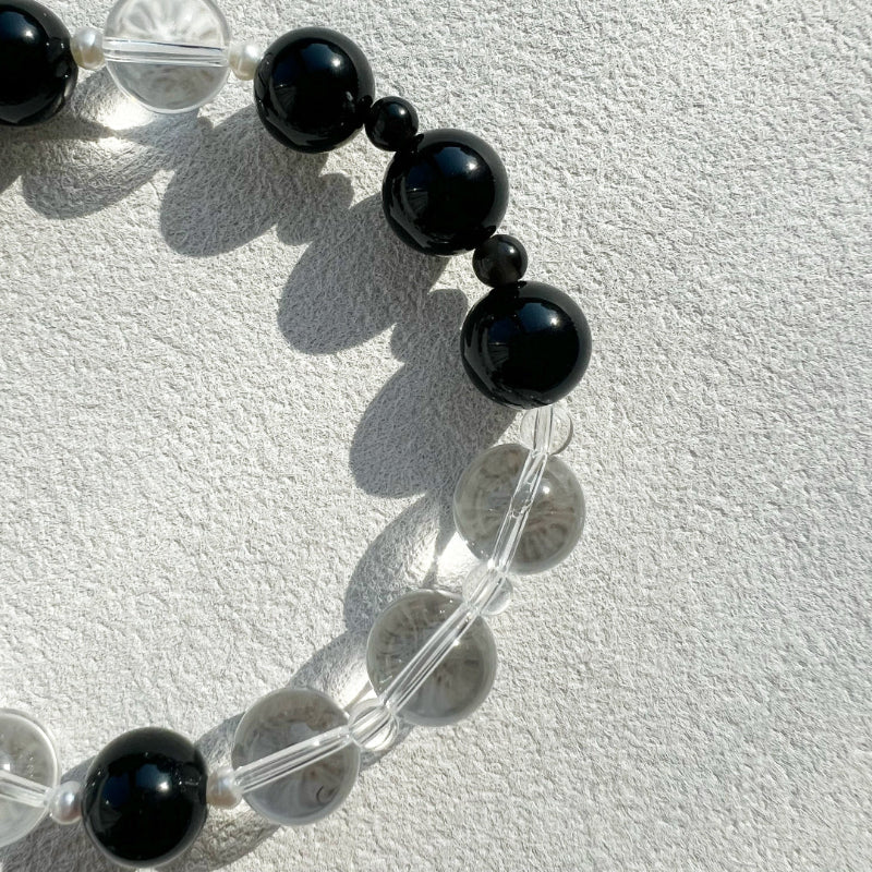 Macro shot of the Yinyang necklace highlighting the rhythmic chiaroscuro between protective black obsidian and light-amplifying clear quartz gemstones.