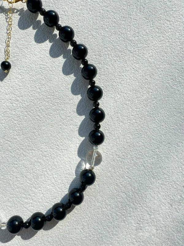 Macro detail of the 10mm natural black obsidian stone on the Yinyang necklace, representing grounding energy and protective shadow.