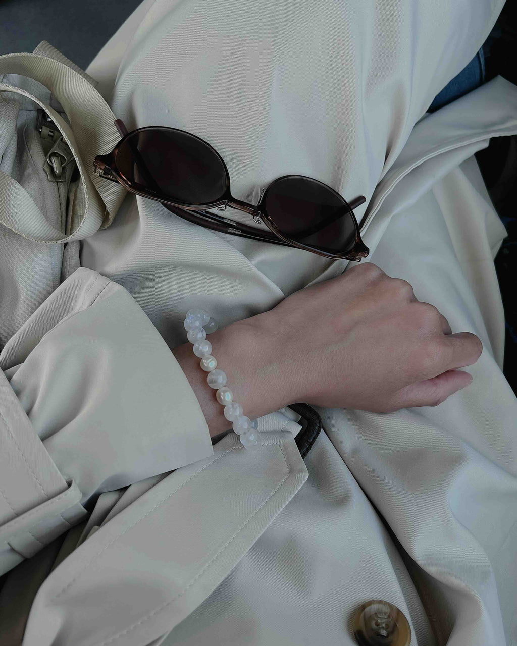 Hand wearing Amaré Blue Moonstone Bracelet styled with a beige trench coat and sunglasses, showcasing the crystal’s soft glow and elegant design.